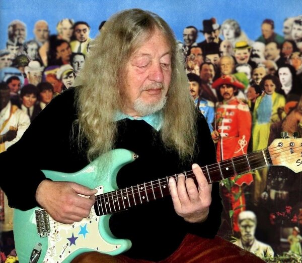 Ein Bild eines Mannes, der Gitarre spielt. Im Hintergrund sieht man Menschen, die ihm zuh&ouml;ren.